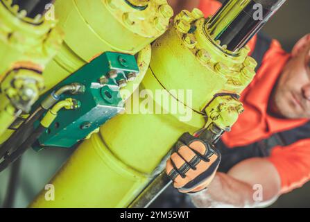 A worker is focused on adjusting hydraulic machinery components using a wrench while in a well-lit industrial facility. Stock Photo