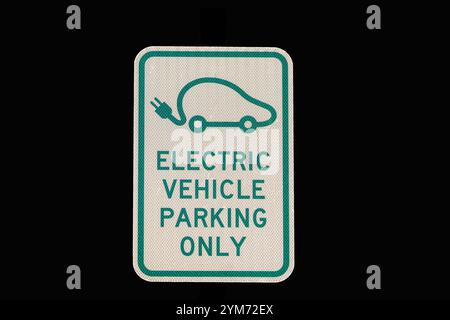 photo of Electric Vehicle Parking Only Sign green letters on off white sign is isolated on black Stock Photo