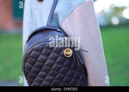 Woman with wooden keychain in shape of smiley face and black leather decor on her backpack outdoors, closeup Stock Photo