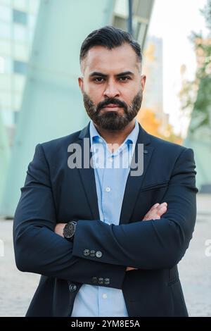 Vertical. Confident and serious businessman with arms crossed posing outdoors, wearing a suit. Turkish or Indian mature male with pensive attitude, representing success and professionalism. High quality photo Stock Photo