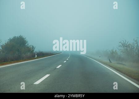 Empty countryside road covered in fog in cold autumn morning, bad weather conditions for driving, selective focus Stock Photo