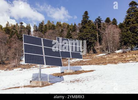 Solar panels in mountains. Photovoltaic modules on top of rock. Snowy forest. Alternative energy sources. Solar collectors generate heat for heating, Stock Photo