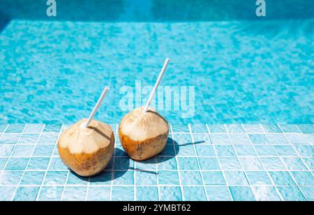 Close-up of two coconuts with straws on the side of the pool. Delicious natural cocktails on the background of clear blue water. Bright sunlight and t Stock Photo