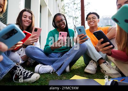 Multiethnic group of students gathering outside sitting on the ground using phones together. Stock Photo