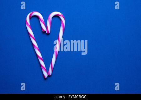 Candy canes arranged in a heart shape against a vibrant blue background, conveying a festive and cheerful atmosphere. Stock Photo