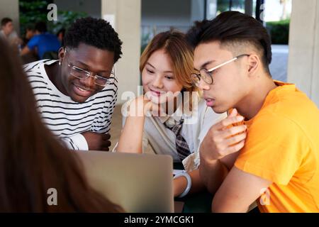 Group of Young People Sitting Around a Table using a laptop to work together in a group project. Stock Photo