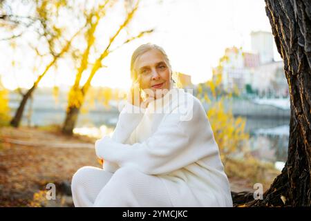 Portrait of woman in white sweater sitting by river in autumn Stock Photo