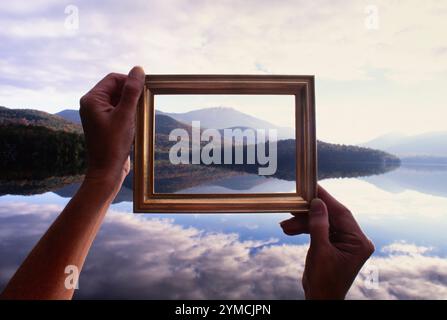 Woman's hands holding picture frame up to calm Lake Placid and hills Stock Photo