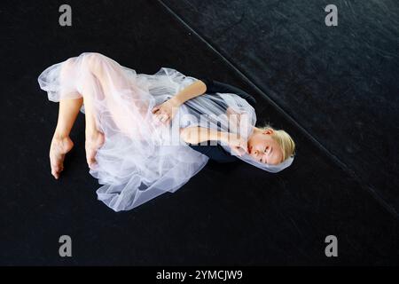 Portrait of ballerina wrapped in white tulle lying on floor in ballet studio Stock Photo