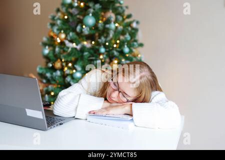 Sleepy woman employee working in office with documents and laptop during Christmas time Stock Photo