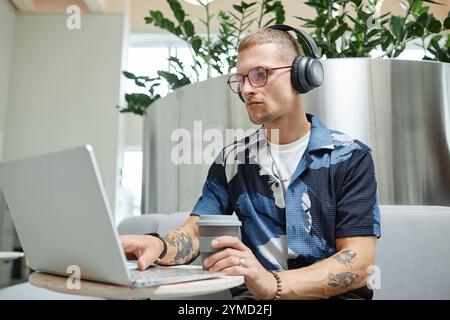 Medium shot of concentrated businessman in headphones typing on laptop working Stock Photo