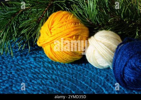 Three balls of wool yarn against the background of a green Christmas tree. Wool blend yarn for knitting warm clothes for the winter. Stock Photo