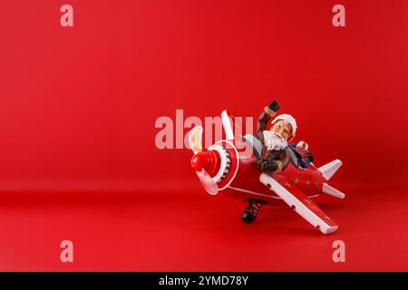 a festive figurine of Santa Claus riding a red toy airplane. background is a solid red color, which complements the festive theme of the figurine. a p Stock Photo