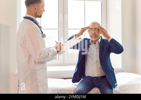 Sick senior man sitting on couch at doctor's office suffering from headache or having migraine. Stock Photo