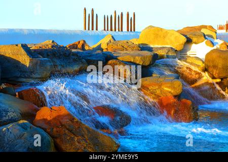 Small waterfall cascading over a series of large, smooth rocks. The water appears to flow from dam or spillway, as indicated by the white wall in the Stock Photo