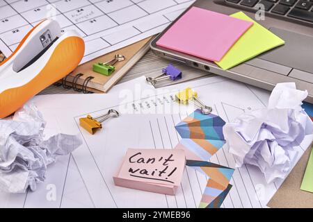 Close-up sticky notes with cant wait handwriting and office stuff. Work papers with charts and stapler. Sticky notes on the laptop Stock Photo