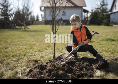 Six-year-old boy in the garden plants tree during sunny spring day. Stock Photo