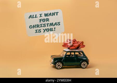 Green toy car with a red bow on top of it. The car is surrounded by a speech bubble that says All I want for Christmas is you Stock Photo