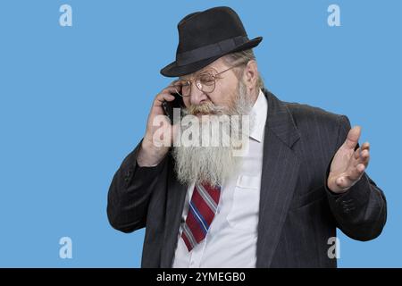Happy bearded senior man talking on phone. Isolated on blue Stock Photo
