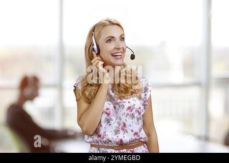 Portrait of smiling blondie wearing headset in office. Female customer support operator Stock Photo