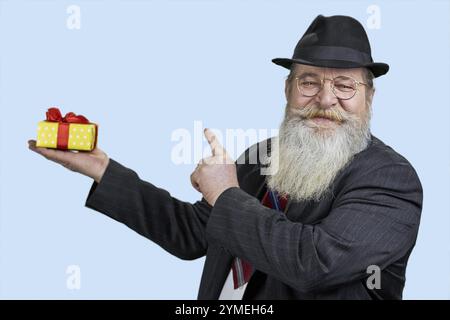 Happy senior bearded man pointing at gift box in another hand. Isolated on blue Stock Photo
