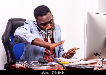 businessman in jacket sitting at desk talking on the phone while holding cellphone. Stock Photo