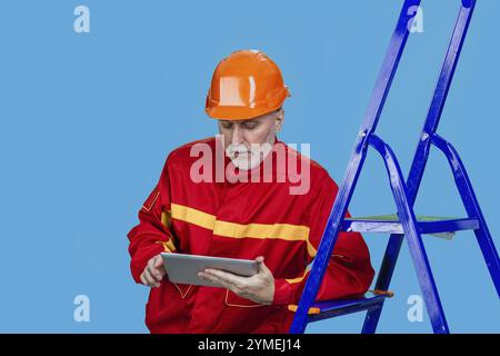 Serious senior male factory or construction worker using a digital tablet. Isolated on blue Stock Photo