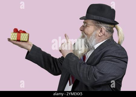 Happy senior bearded man smiling while holding gift box. Isolated on pink Stock Photo