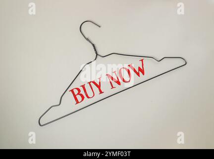 Clothes hanger with the words Buy Now written on it. The hanger is hanging on a white background Stock Photo