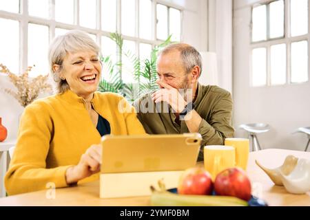Senior couple laughing while using digital tablet at home Stock Photo