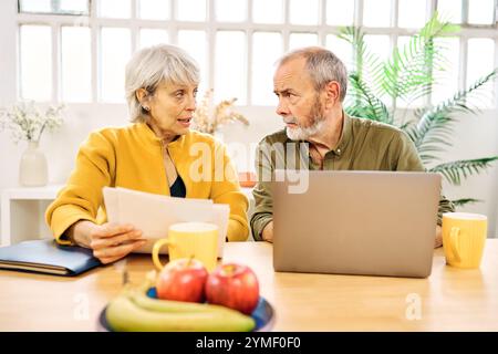 Senior couple discussing documents and working on laptop at home Stock Photo
