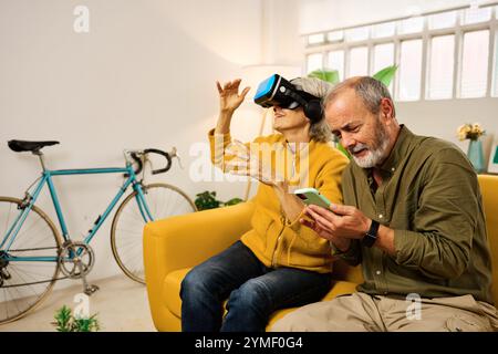 Senior couple exploring virtual reality and using smartphone at home Stock Photo