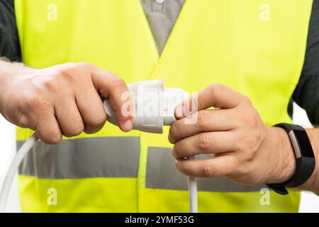 Close-up of male electrician trades worker wearing fluorescent vest plugging in socket on extension cord isolated on white studio background Stock Photo