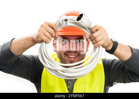Male trades industry worker electrician smiling with friendly expression wearing vest and orange hardhat safety equipment holding white extension cord Stock Photo