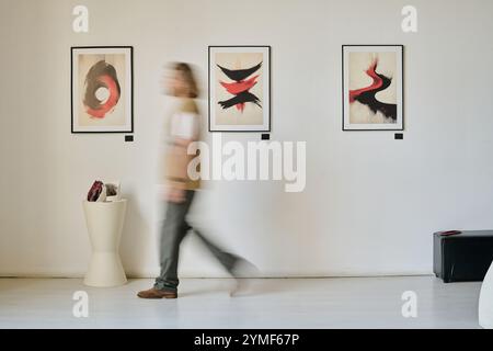 Blurred figure walking through art gallery exhibiting abstract paintings on wall demonstrating motion. Artwork showcasing dynamic brushstrokes and vivid contrasts Stock Photo