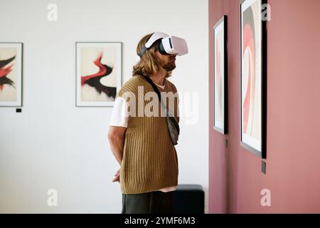 Man engaging with art gallery exhibit while wearing virtual reality headset. Exhibiting interest in immersive digital experience enhancing appreciation of artwork Stock Photo
