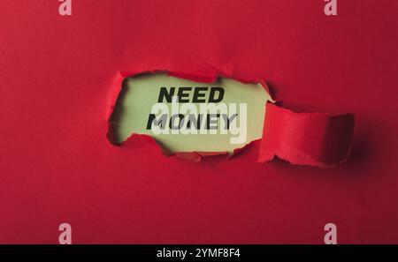 Red background with a torn piece of paper with the word NEED MONEY written on it. The torn paper is in the middle of the image Stock Photo