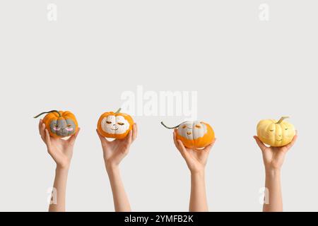 Female hands holding pumpkins with drawn faces and clay masks on white background Stock Photo