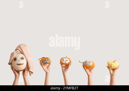 Female hands holding pumpkins with drawn faces and clay masks on white background Stock Photo