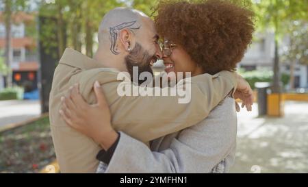 Interracial couple embracing lovingly in a sunny urban park, depicting joy and diversity. Stock Photo