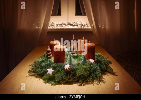 First advent with orange brown candles on an advent wreath made of green fir branches and christmas decoration on a table by the window in warm light, Stock Photo