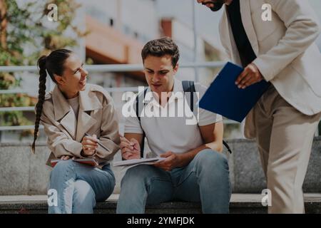 High school students collaborating outdoors with teacher assistance Stock Photo