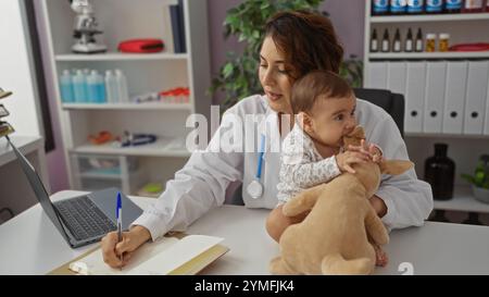 Pediatrician woman working indoors in a clinic examines a baby with toddler toys while taking notes, highlighting female healthcare interaction in a m Stock Photo