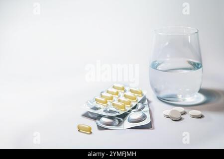 Pills and capsules separately and in blister packs next to a glass with water, medication on a light gray background, medicine and health concept, cop Stock Photo