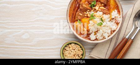 Delicious massaman curry with beef, potatoes, rice, and peanuts on white wooden background, traditional thai cuisine, space for text Stock Photo