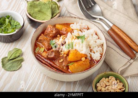 Bowl of delicious massaman curry with rice and peanuts on white wooden background, dish of thailand Stock Photo
