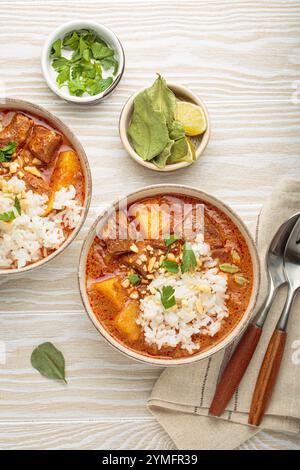 Two bowls of delicious massaman curry with beef, potatoes, rice, and peanuts, garnished with parsley on white wooden background, Thai cuisine Stock Photo
