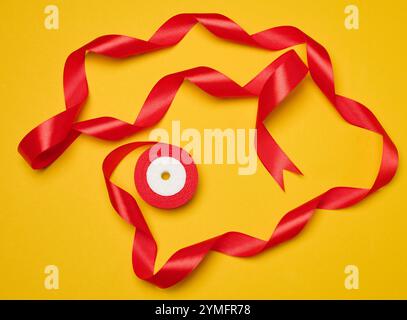 Spool of red silk ribbon on yellow background, top view Stock Photo