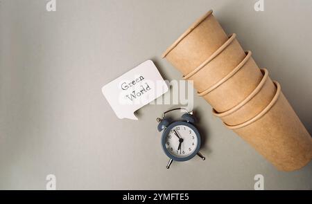 Clock sits on a table next to a stack of paper cups and a sign that says Green World. Stock Photo