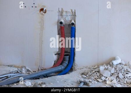 Wall plumbing system installation with exposed red and blue water pipes and drainage components during home renovation Stock Photo